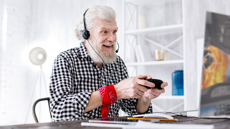 Ein älterer Mann mit weißen Haaren sitzt am PC und hält einen Kontroller